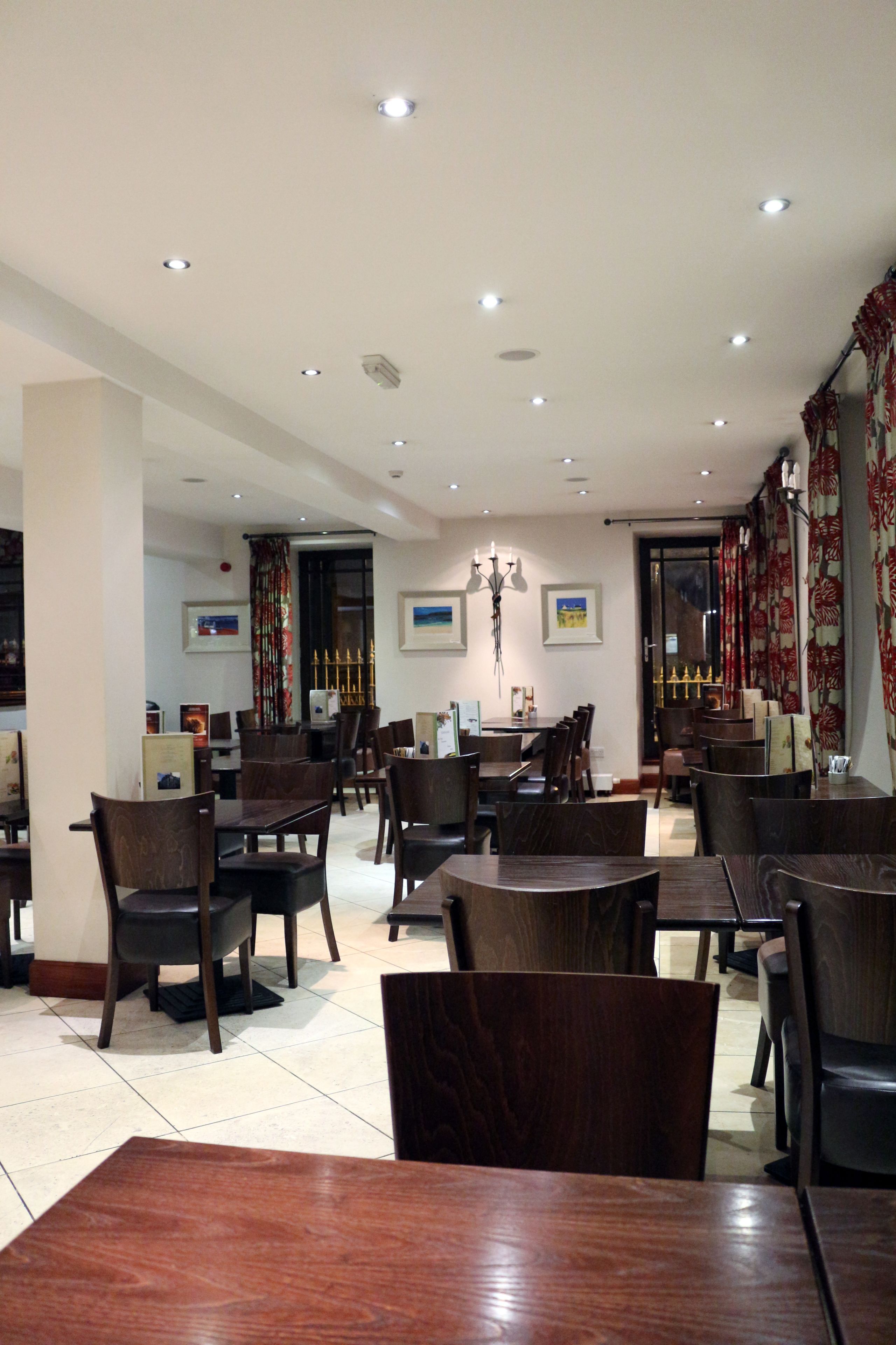 A restaurant with wooden tables and chairs, recessed ceiling lights, and framed pictures on the walls.