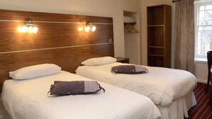 A hotel room with two beds, wooden headboard, bedside lamps, and a window with curtains. - County Hotel (Stornoway)
