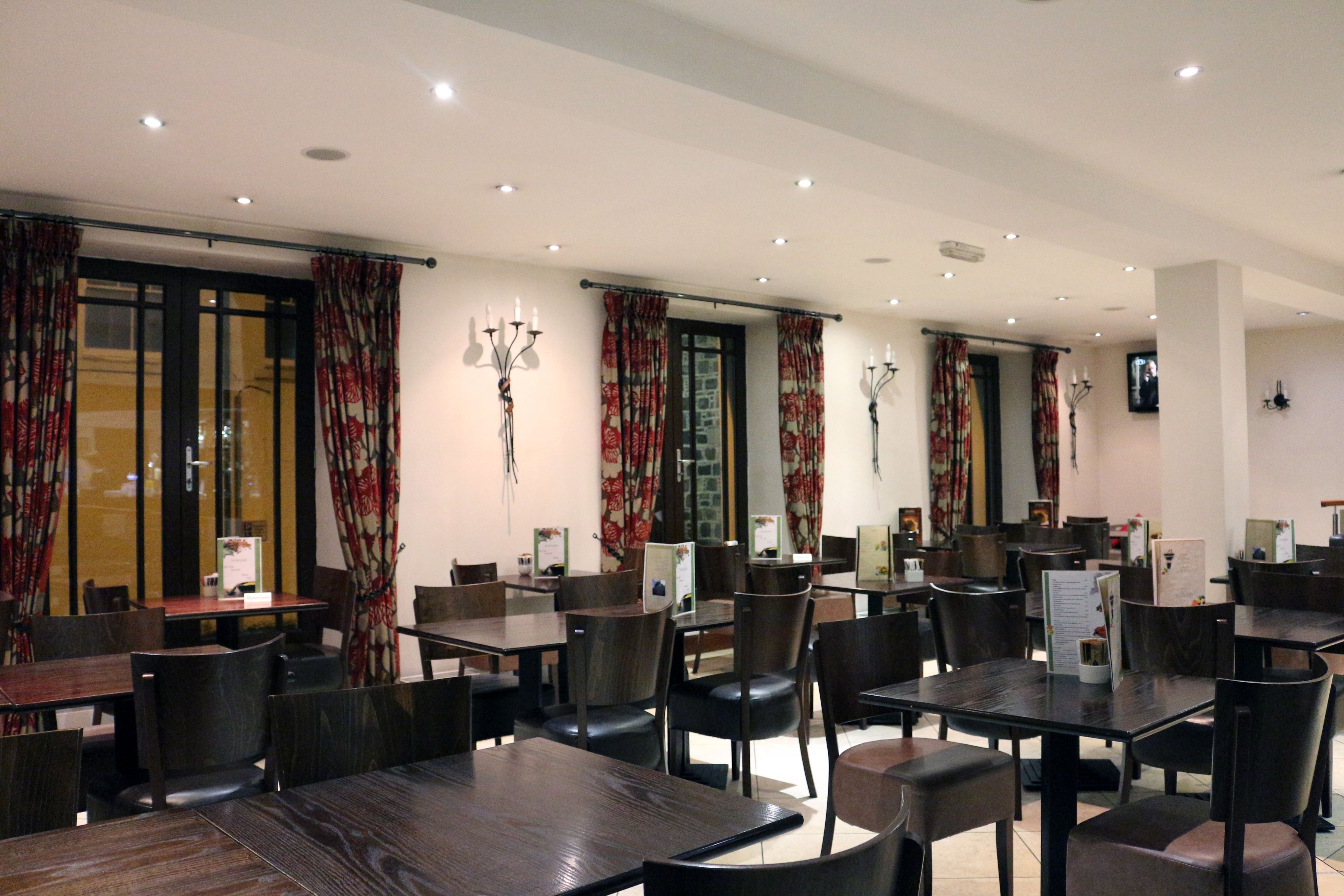 Un restaurant doté de nombreuses tables et chaises, d’un mur en pierre et de rideaux à motifs floraux.