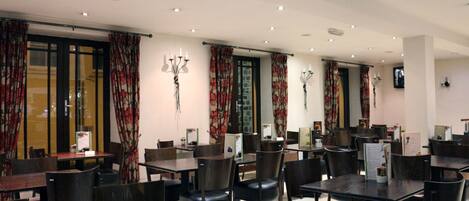Un restaurant doté de nombreuses tables et chaises, d’un mur en pierre et de rideaux à motifs floraux.