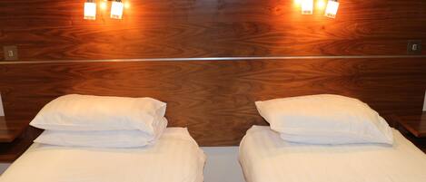 Habitación de hotel con dos camas individuales, cabecera de madera y lámparas de lectura fijadas a la pared.