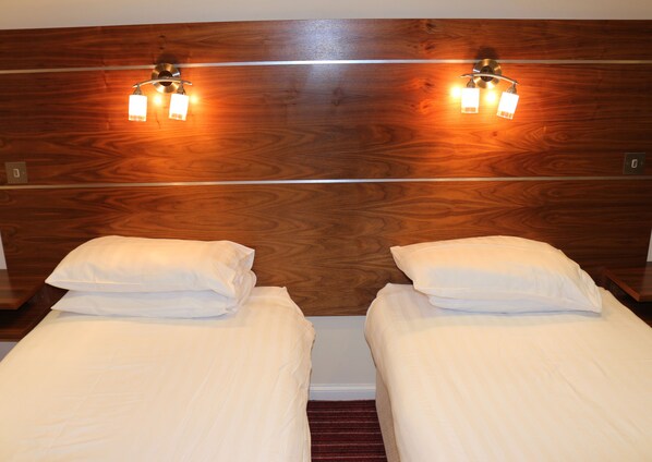 A hotel room with two single beds, wooden headboard, and wall-mounted reading lights. - County Hotel (Stornoway)