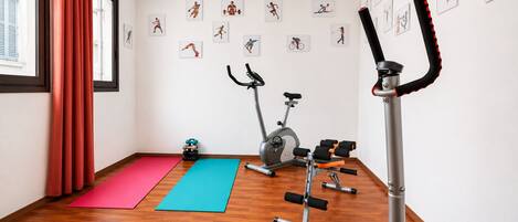 A gym with exercise equipment, exercise mats, and artwork on the walls.