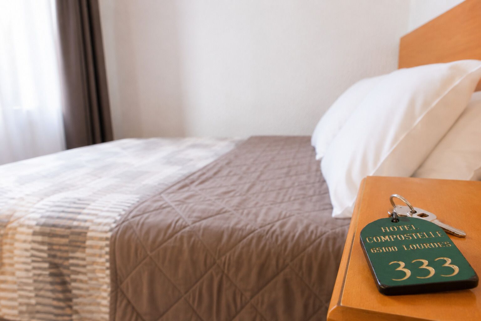 Habitación de hotel con cama, mesita de noche y llavero con el nombre del hotel y número de habitación.