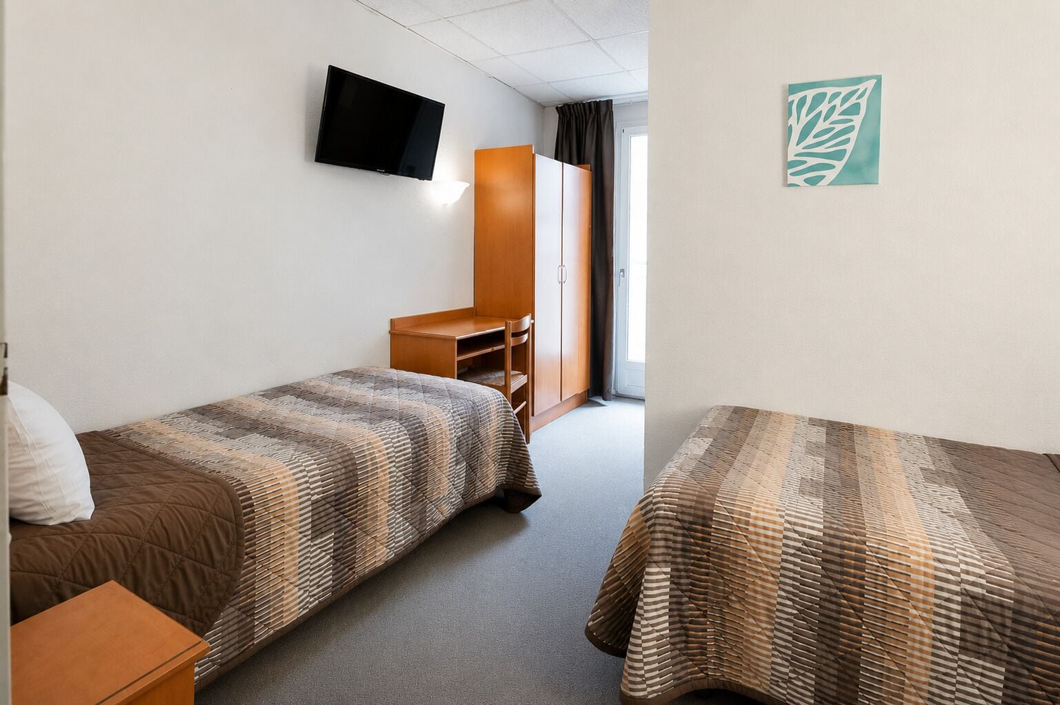 Une chambre d’hôtel avec deux lits, une télévision, une armoire et un bureau.