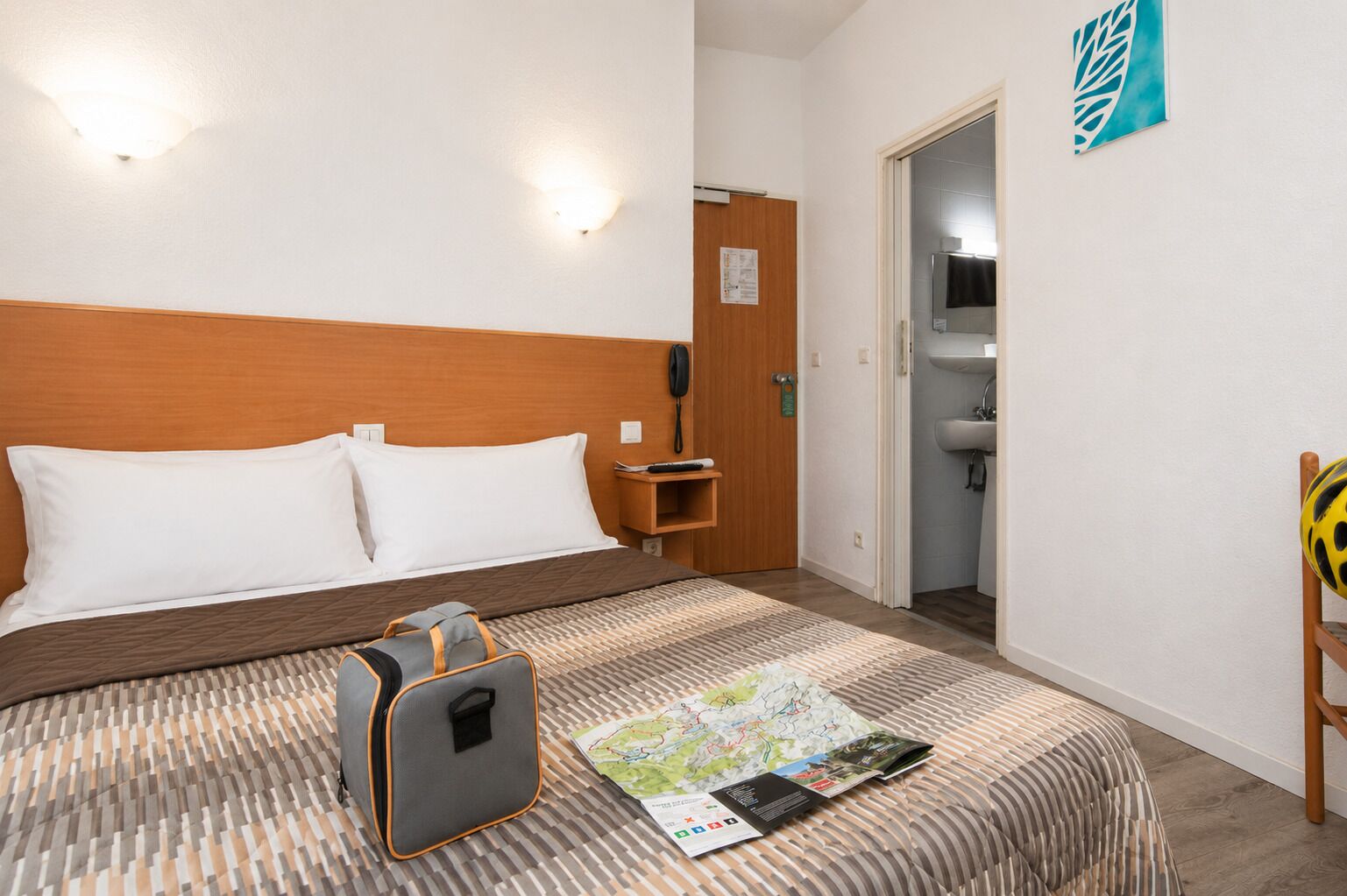 Une chambre d’hôtel avec un lit, une table de chevet avec un téléphone, une carte, un sac et une salle de bain visible à travers une porte ouverte.