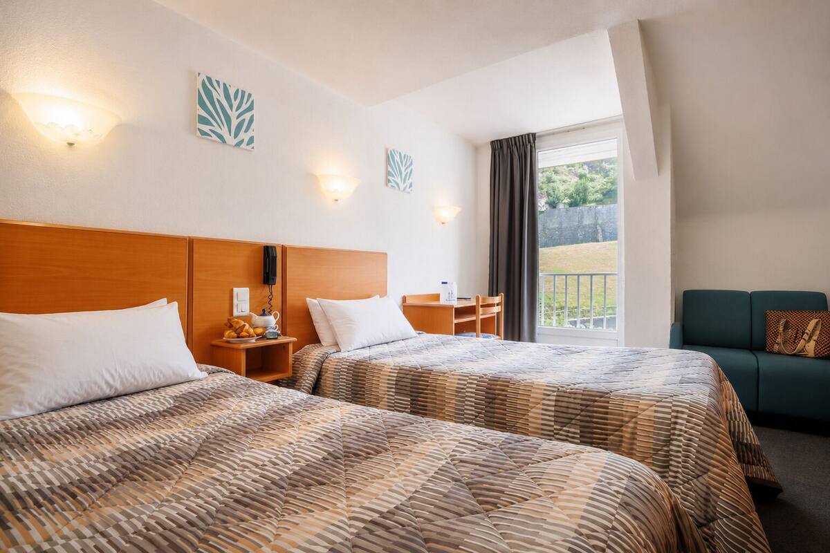 A hotel room with two beds, a desk, a chair, a sofa, and a balcony with a view.