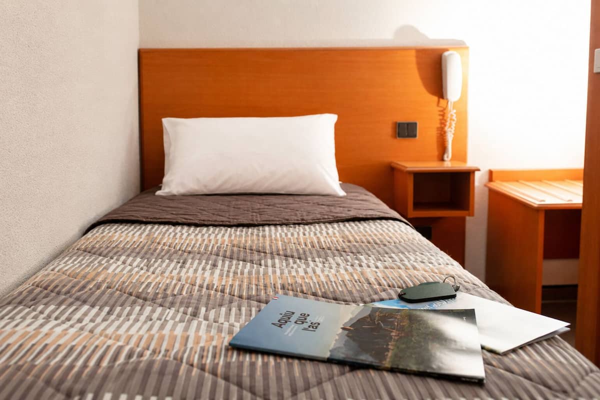 A hotel room with a bed, a bedside table, a lamp, and a magazine on the bed.