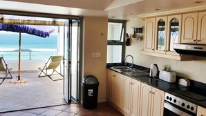 A kitchen with a view of the ocean, a trash bin, and a dining area with chairs. - On the Beach 1, Langebaan 2-Sleeper (Langebaan)