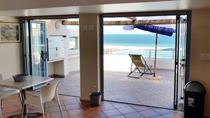 A room with a view of the beach, a table with chairs, a trash bin, and a ceiling fan. - On the Beach 1, Langebaan 2-Sleeper (Langebaan)