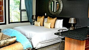A bedroom with a large bed, a desk, a mirror, and a window with blinds.