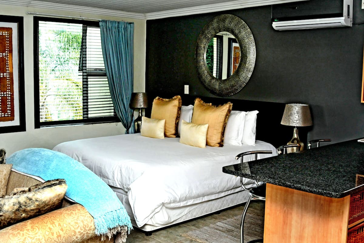 A bedroom with a large bed, a desk, a mirror, and a window with blinds.