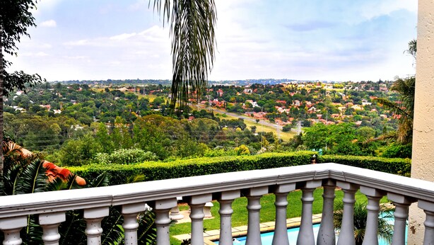 A balcony with a view of a residential area, a swimming pool, and lush greenery.