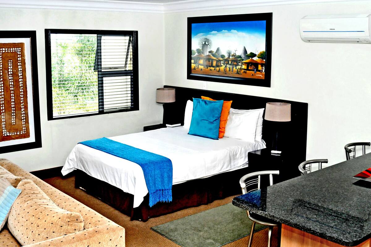 A hotel room with a bed, a desk, a chair, a TV, and an air conditioner.