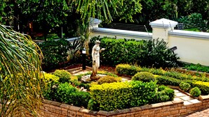 A well-maintained garden with a statue, neatly trimmed hedges, and a brick wall.