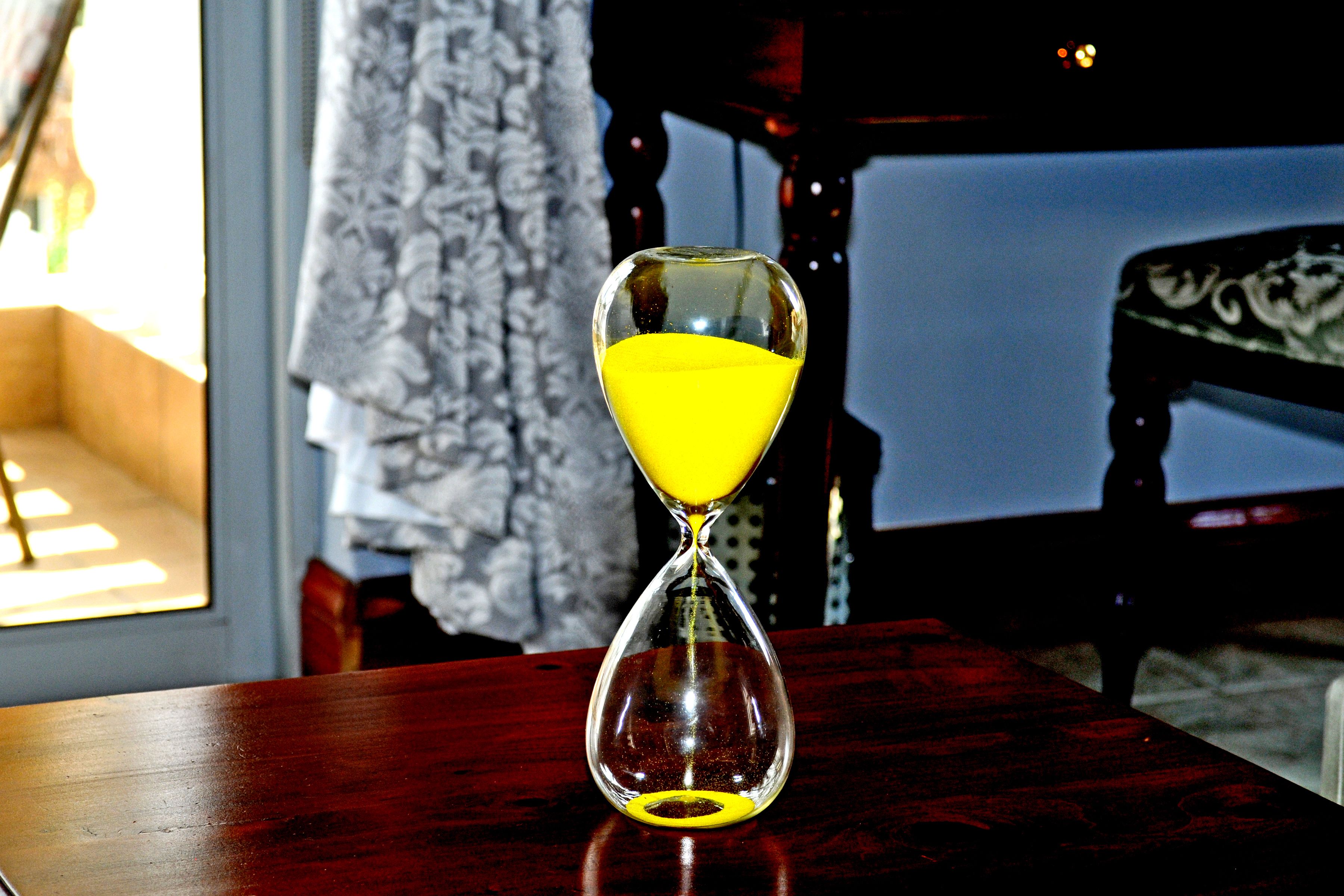 Un reloj de arena sobre una mesa de madera con una ventana al fondo.