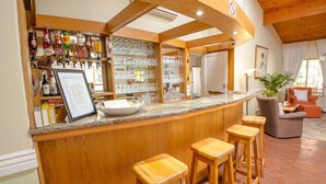A bar area with a wooden counter, stools, and a variety of bottles. - Avalone Guest House (St. Lucia)