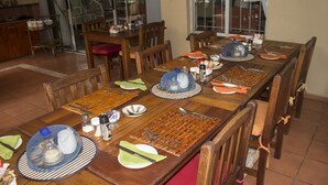A dining area with wooden tables set for a meal, including plates, cutlery, and condiments. - Avalone Guest House (St. Lucia)