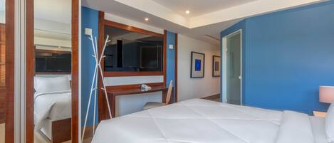 A hotel room with a large bed, a desk with a chair, a mirror, and a wardrobe.