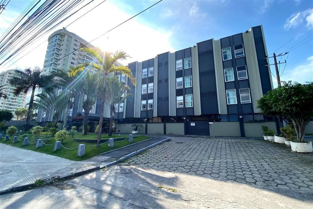 Un edificio moderno con techo plano, múltiples ventanas y un acceso pavimentado con plantas en macetas.