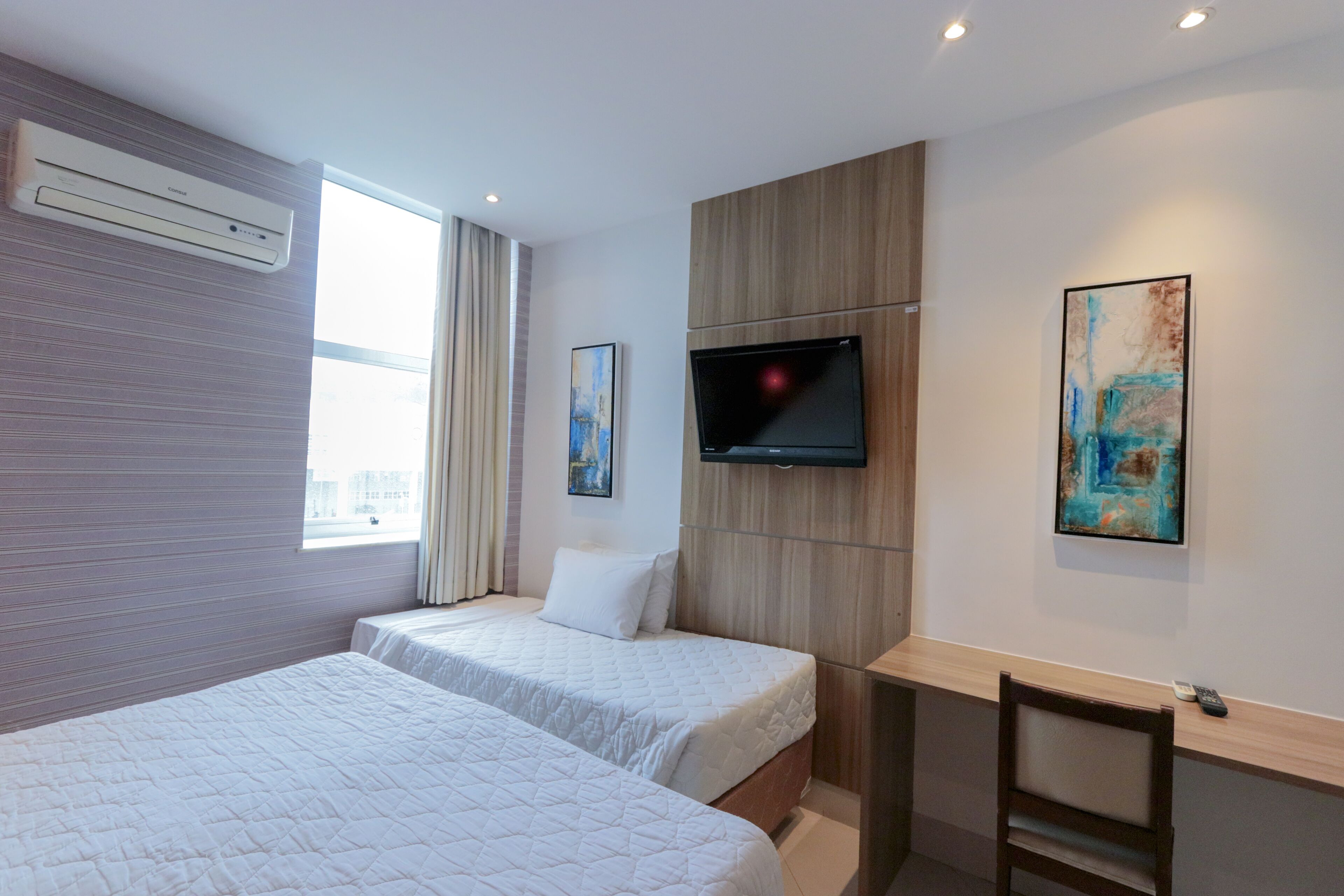 Une chambre d’hôtel avec deux lits, un téléviseur à écran plat, une fenêtre avec des rideaux et des œuvres d’art accrochées aux murs.