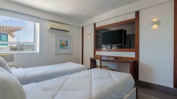 Habitación de hotel con dos camas, televisión, escritorio y ventana con aire acondicionado.