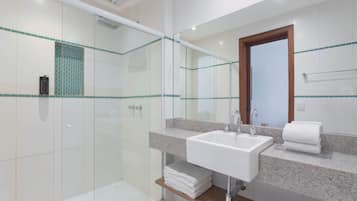 A modern bathroom with a glass shower enclosure, a sink with a marble countertop, and a wooden shelf with folded towels.