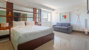 A modern hotel room with a large bed, a grey sofa, a large window, and a painting on the wall. - DOM Barra Hotel (Rio de Janeiro)