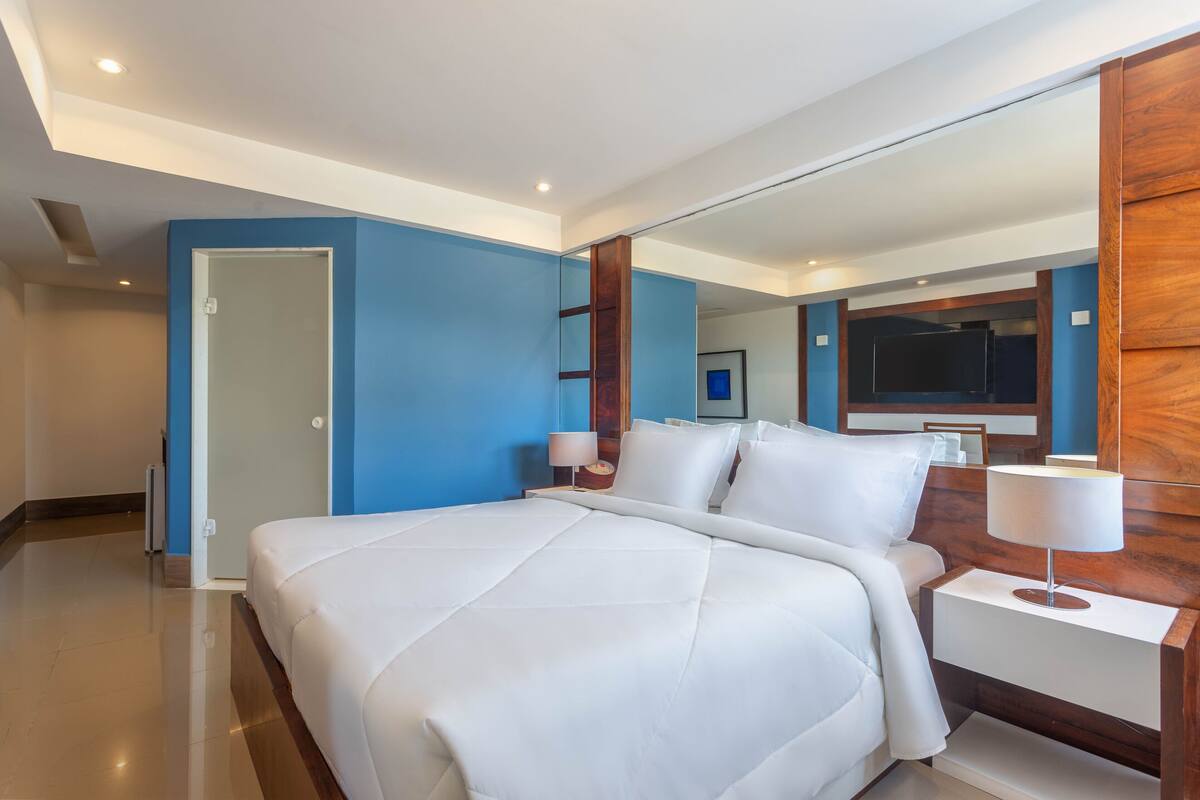 A hotel room with a large bed, a wooden nightstand, a mirror, and a TV.