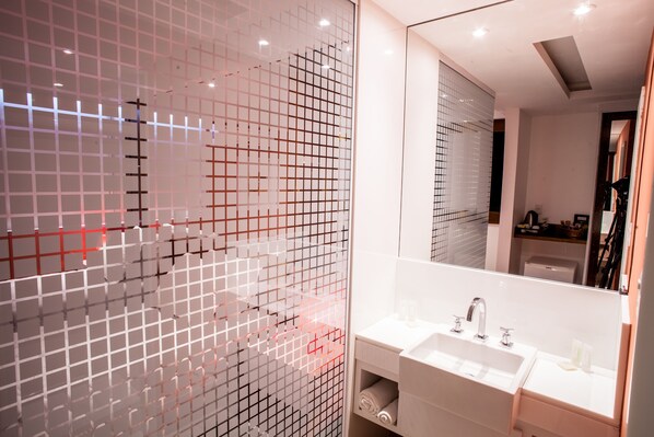 Une salle de bain moderne avec un grand miroir, un lavabo blanc et une cloison en verre à motifs géométriques.
