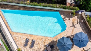 A rectangular swimming pool with tiled edges, surrounded by a stone patio. There are two lounge chairs and two umbrellas on the patio. - DOM Barra Hotel (Rio de Janeiro)