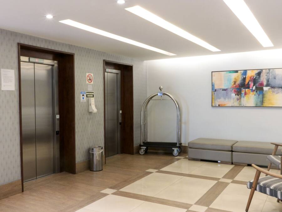 A lobby with two elevators, a trash bin, a cart, a sofa, and a colorful abstract painting on the wall.