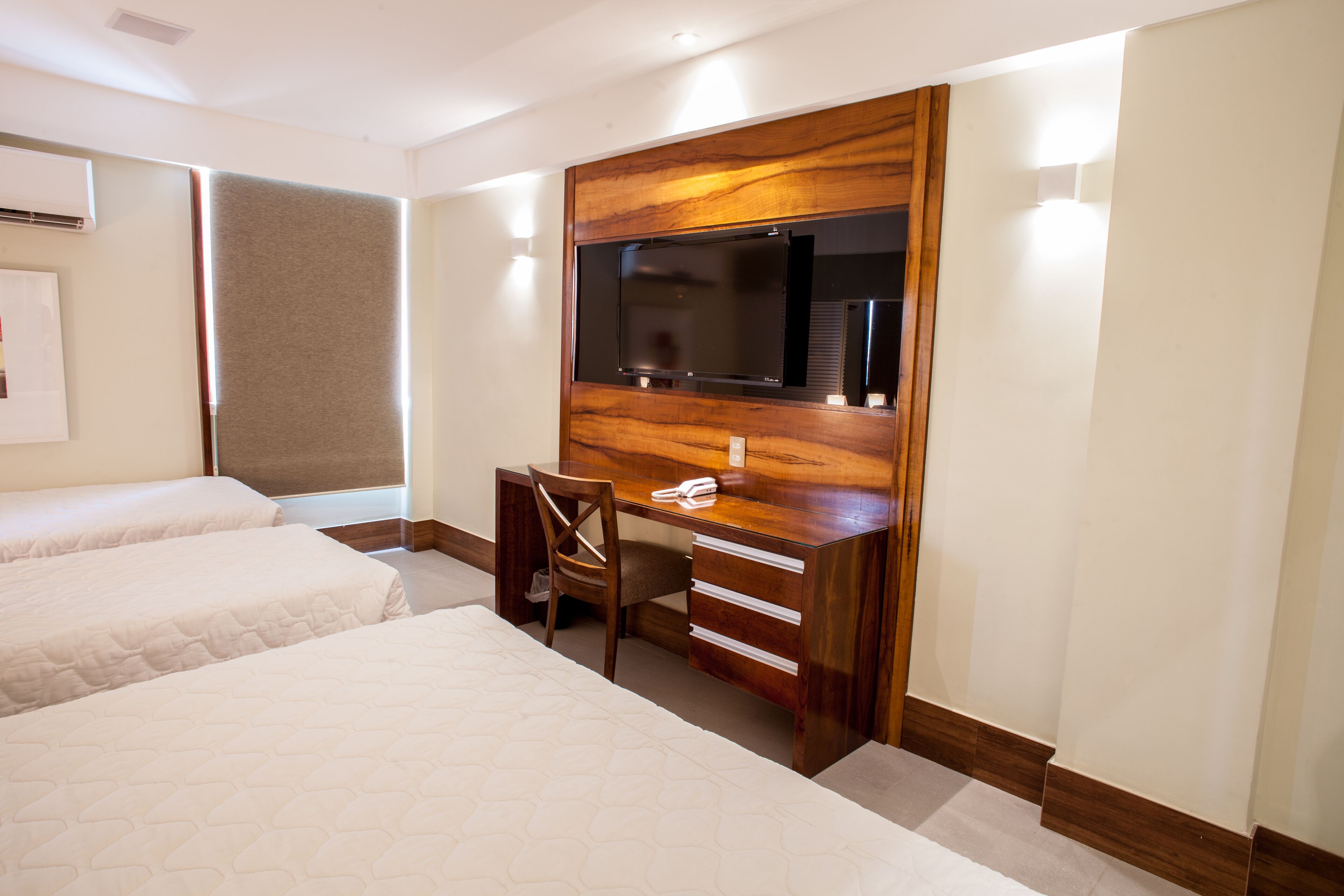 Habitación de hotel con dos camas, un escritorio, una silla, un televisor y aire acondicionado instalado en la pared.