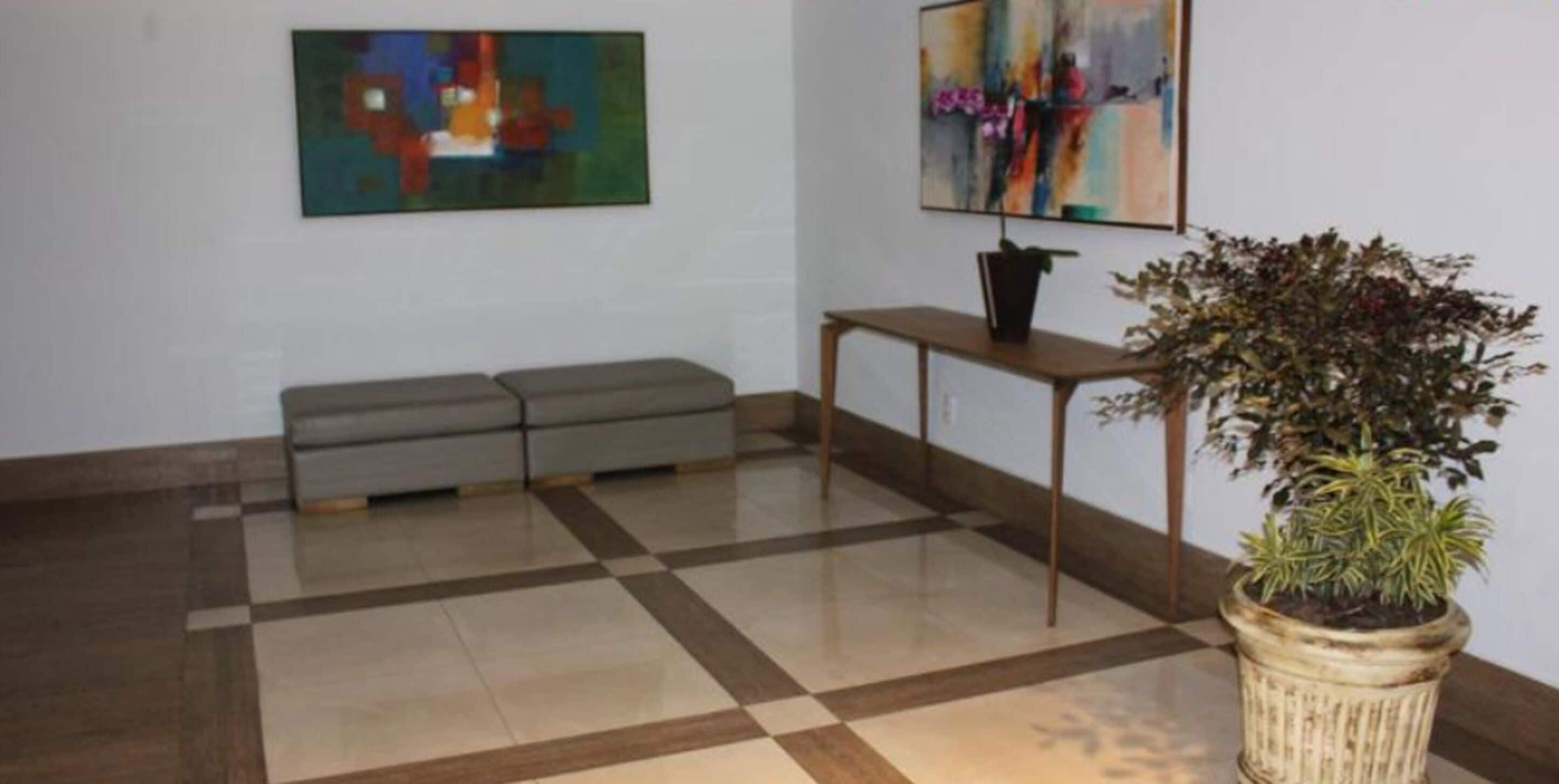 Eine Lobby mit einem Schachbrettmuster-Boden, einem grauen Sofa, einem kleinen Tisch mit einer Pflanze und abstrakten Gemälden an den Wänden.