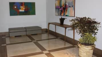 Eine Lobby mit einem Schachbrettmuster-Boden, einem grauen Sofa, einem kleinen Tisch mit einer Pflanze und abstrakten Gemälden an den Wänden.