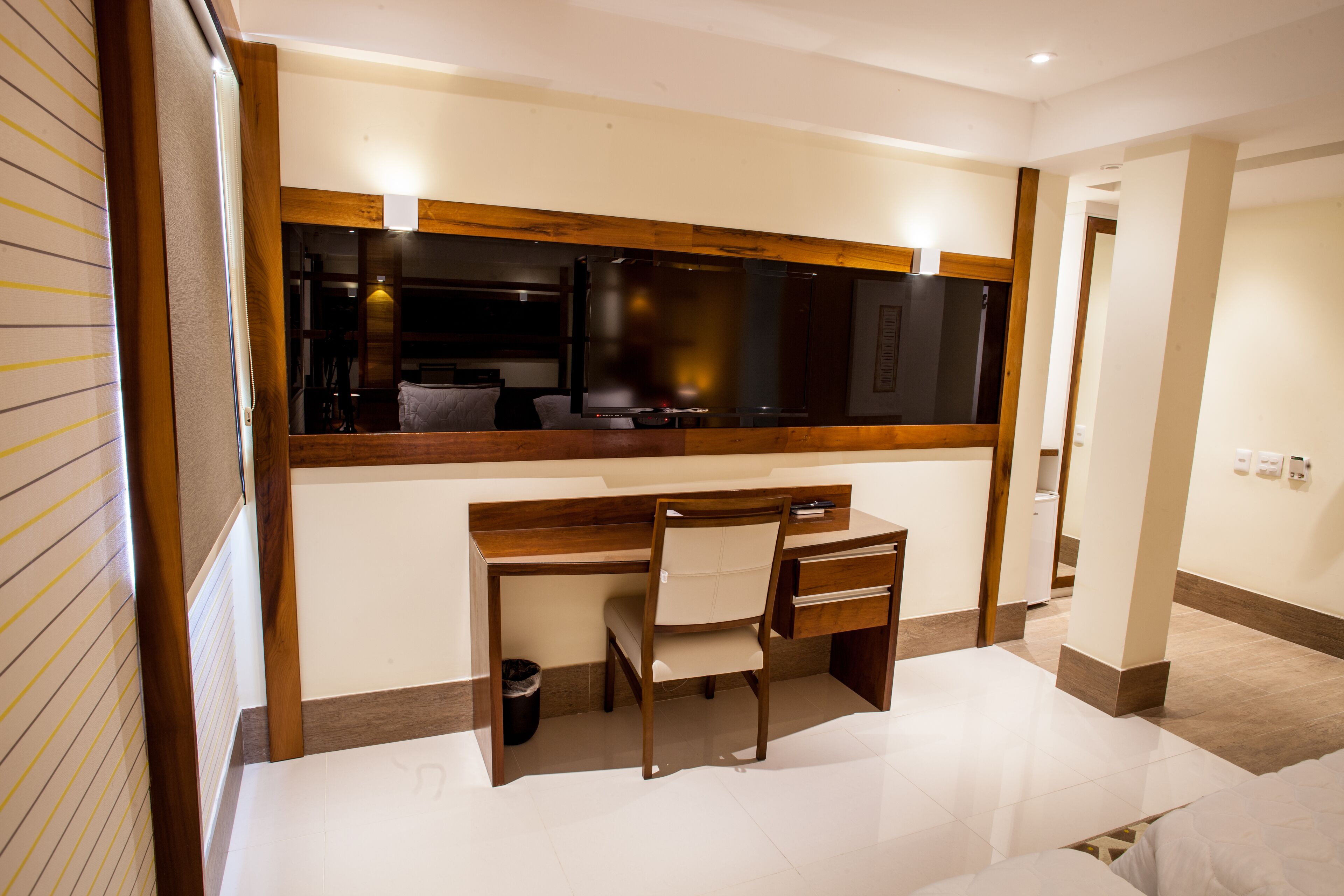 A hotel room with a wooden desk, a chair, a large mirror, and a bed.