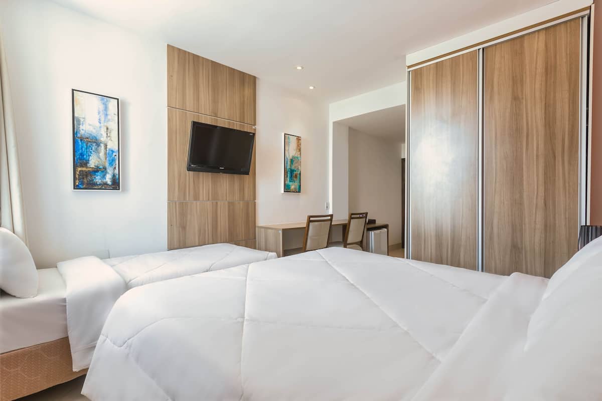A modern hotel room with a large bed, two bedside tables, a TV mounted on the wall, and a wooden wardrobe.
