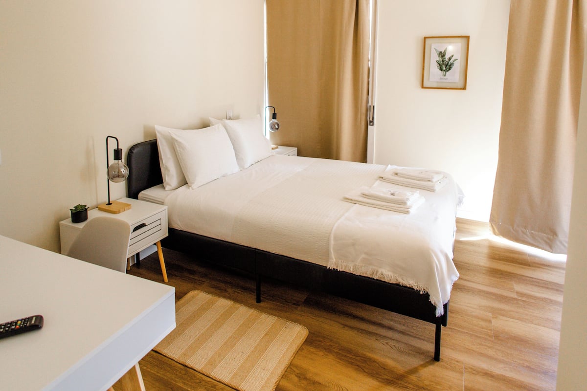 A bedroom with a bed, bedside table, lamp, and a small desk.