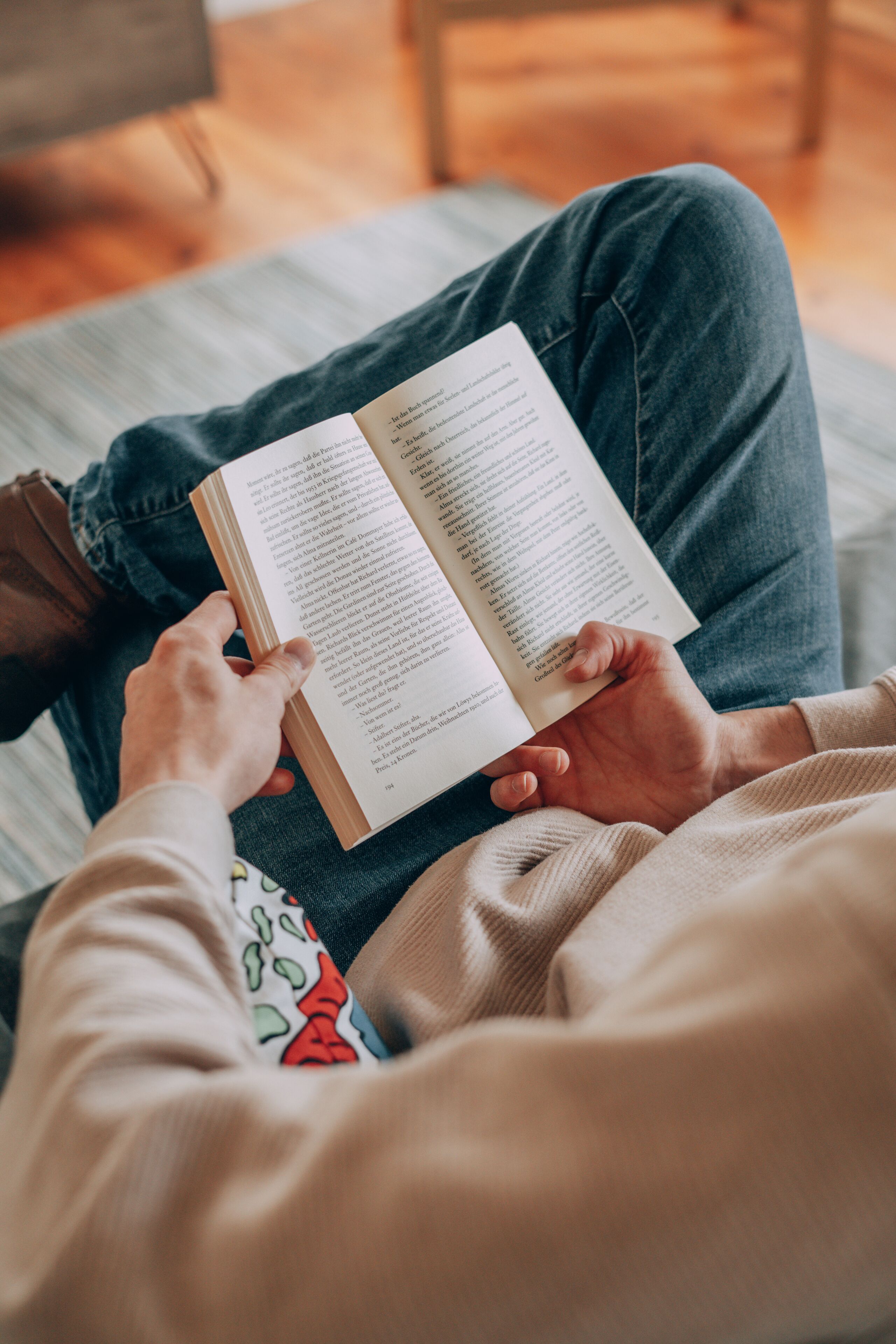 Eine Person sitzt auf einer Couch und hält ein offenes Buch.