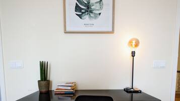 A workspace with a desk, chair, potted plant, books, and a framed artwork on the wall.