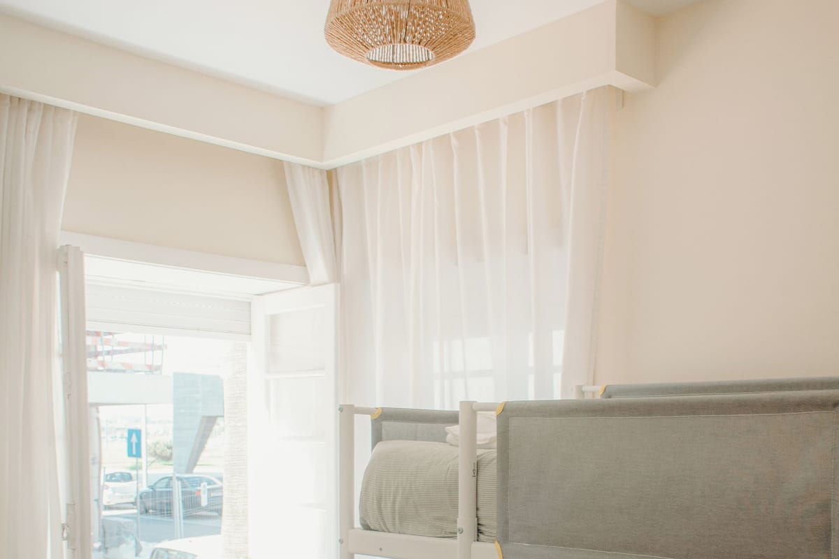 A bunk bed with a grey mattress and a white pillow, a white desk with a chair, and a hanging light fixture.