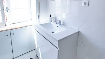 Un baño moderno con tocador blanco, un espejo grande y una ventana que deja entrar luz natural.