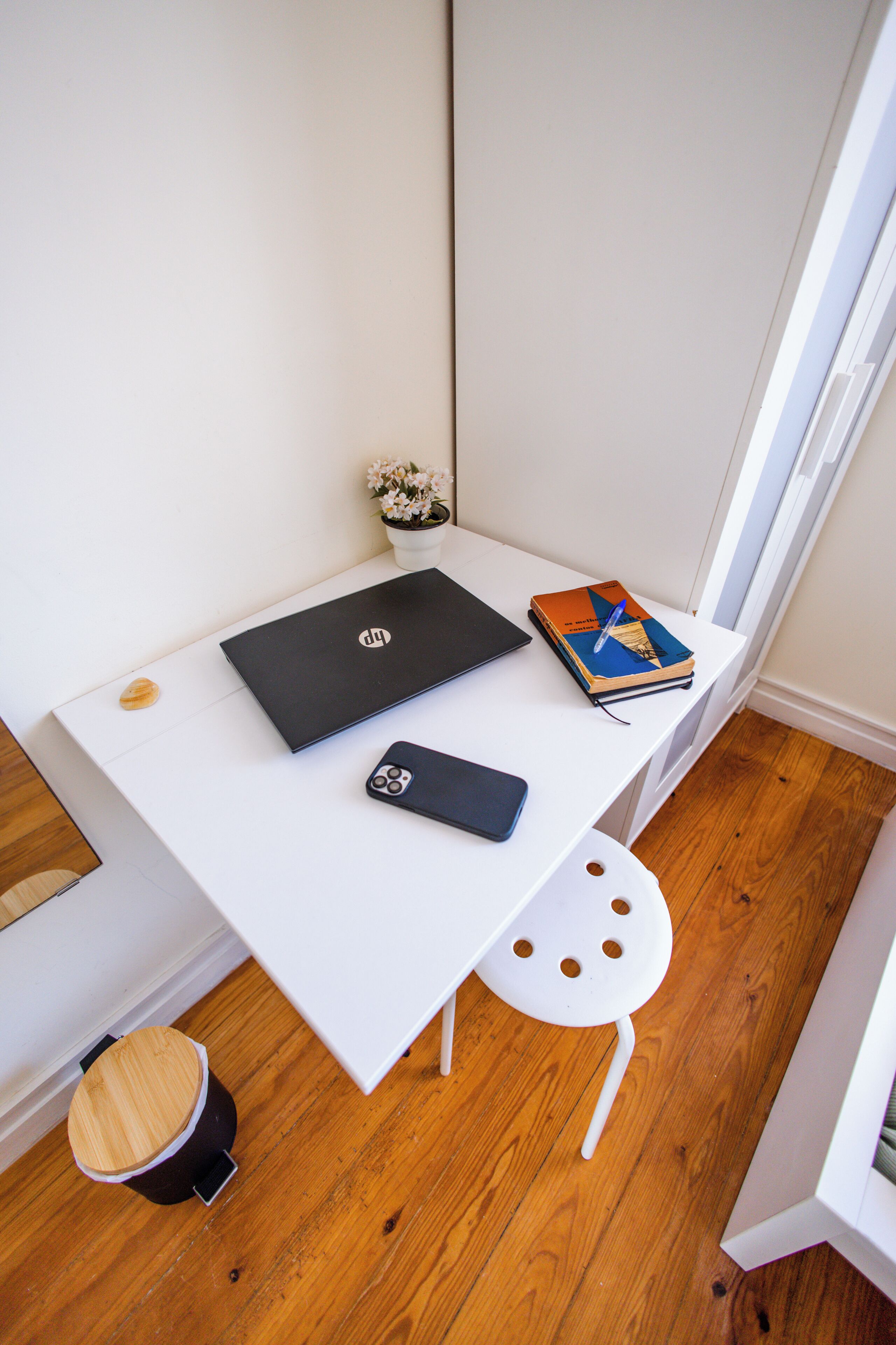 A white desk with a laptop, a smartphone, and a book. There is a small plant on the desk.