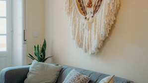 Un salón con un sofá gris, un tapiz de macramé y una planta en maceta.