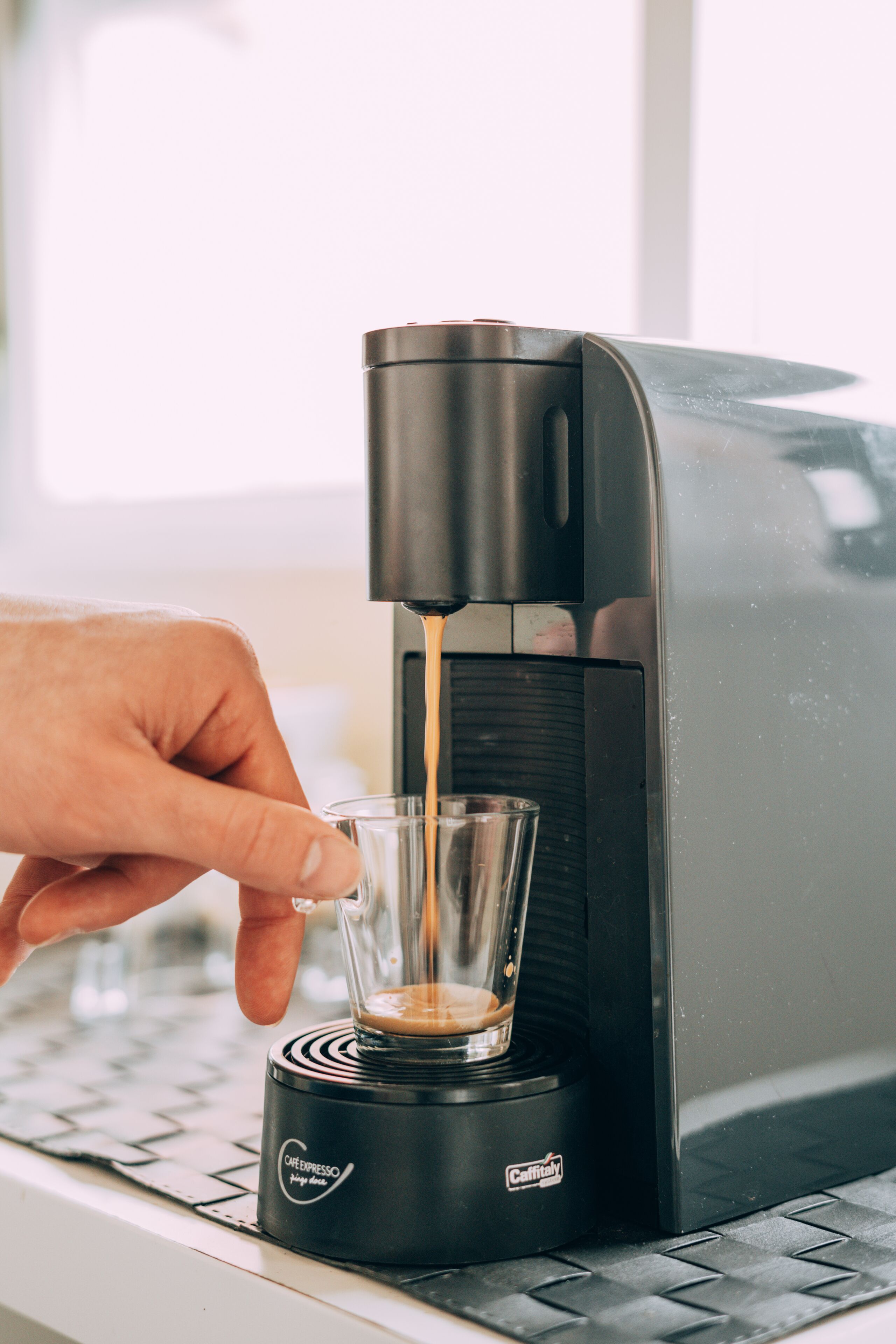Uma mão servindo café em um copo a partir de uma máquina de café expresso Caffitaly.