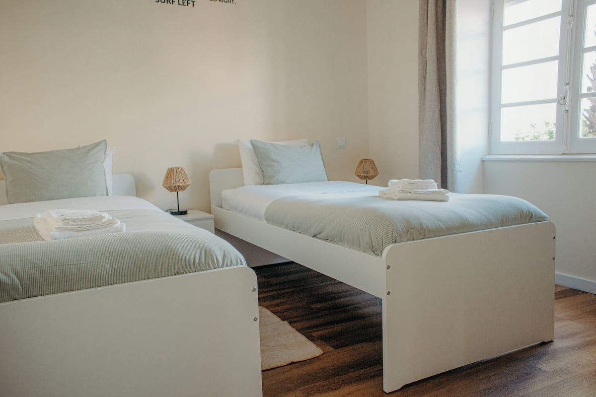 A hotel room with two single beds, a window with curtains, and a wooden floor.