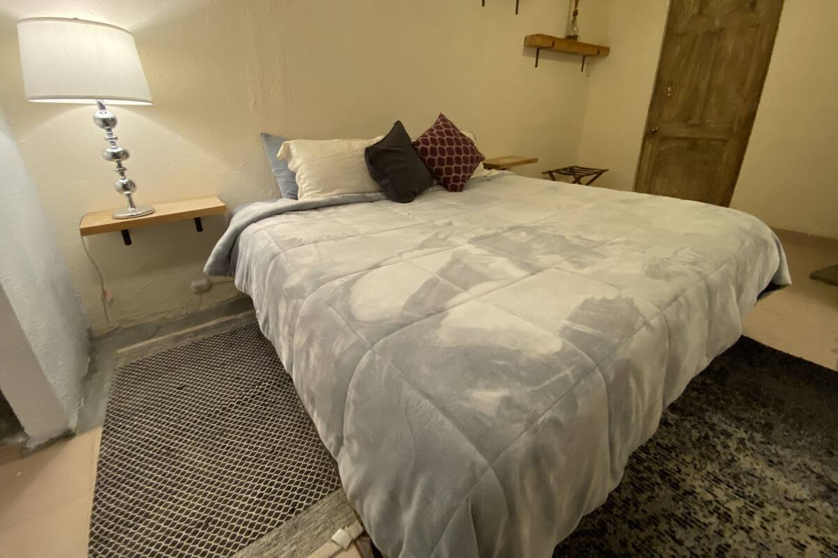 Ein Schlafzimmer mit einem großen Bett, einem Nachttisch mit Lampe, einer kleinen Ablagefläche mit Dekoration und einer Tür.