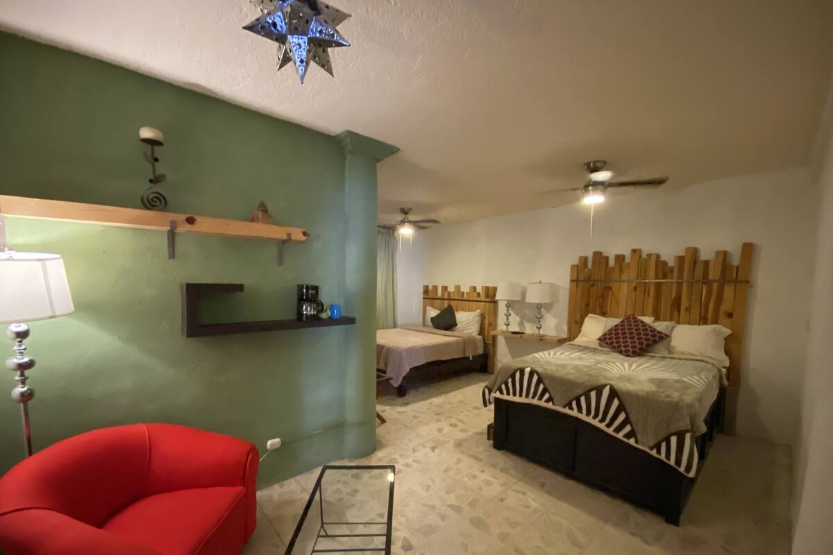 Ein Schlafzimmer mit einem Bett, einem roten Sessel, einer Kaffeemaschine und einem Deckenventilator.