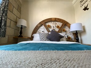 A neatly made bed with a blue bedspread and white pillows, a decorative headboard with sunflowers, and two bedside lamps. - AmaneZer Hotel Boutique (San Miguel de Allende)
