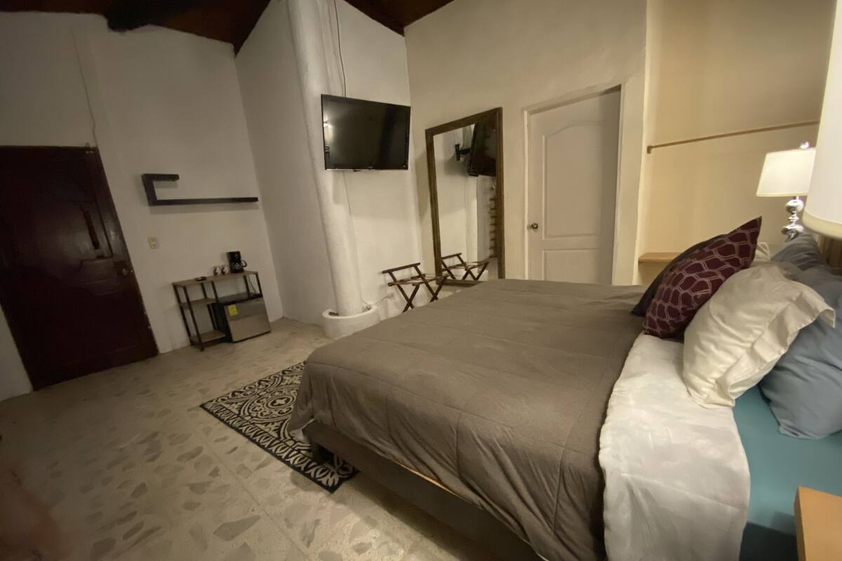 Ein Schlafzimmer mit Bett, einem an der Wand befestigten Fernseher, einer Tür, einem kleinen Tisch und einem Stuhl.